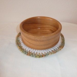 以下が含まれることがあります： ナチュラルな木製の仕上げのウッドボウルが、白、緑、茶色の糸で編まれたかぎ針編みのコースターの上に置かれています
