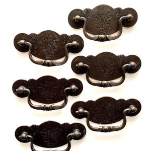 May include: A white ceramic mug with a black handle and the text "But First, Coffee" in a black, bold font. The mug is sitting on a wooden surface. The mug is approximately 4 inches tall.