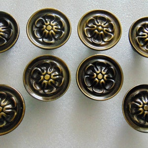 May include: Eight antique brass cabinet knobs with a floral design. Each knob has a raised flower with five petals and a center circle.
