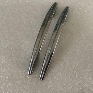 May include: Two chrome-finished, curved metal handles. The handles are elongated and have a smooth, reflective surface. They are likely for a cabinet or drawer, offering a modern aesthetic.