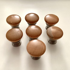 May include: Seven wooden cabinet knobs with a light brown finish and a rounded shape. The knobs are mounted on a silver-colored base. The knobs are arranged in a circular pattern.