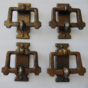 May include: Four antique brass drawer pulls with a hammered finish. Each pull has a rectangular shape with a rounded opening in the center. The pulls are ornate and have a vintage look.