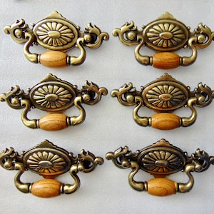 May include: Six antique brass cabinet knobs with a wood center. Each knob has a decorative floral design.