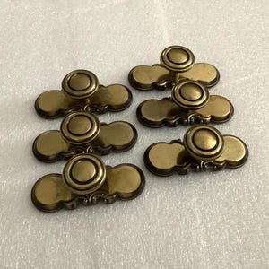 May include: Six antique brass cabinet pulls with a round knob design. Each pull has a rectangular base with decorative detailing. The pulls are arranged on a white surface.