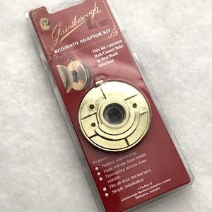 May include: A Gainsborough bed/bath adaptor kit in clear plastic packaging with a red backing card. The kit includes a circular gold-toned metal door hardware component with a central square opening and mounting holes, designed to convert hall/closet sets.