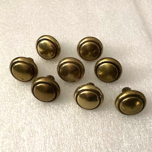 May include: A collection of eight antique brass cabinet knobs. Each knob has a rounded, domed face and a small stem for attachment. The knobs have a warm, aged patina, suggesting they are vintage or vintage-inspired.