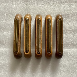 May include: Five wooden cabinet pulls with brass accents. The pulls are rectangular in shape and have a slightly rounded edge. The brass accents are in the center of the pulls and have a slightly raised design.