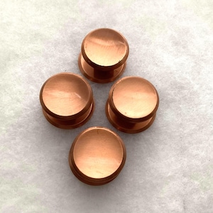 May include: Four circular cabinet knobs with a smooth, polished copper finish. Each knob features a flat, rounded top surface and a cylindrical base, arranged in a diamond formation. The metallic surface reflects light, highlighting the warm, reddish-brown tone of the copper material.