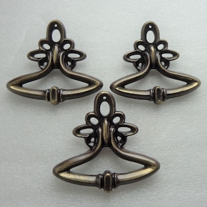 May include: Three antique brass drawer pulls with a decorative floral design. Each pull has a curved, open-top design.
