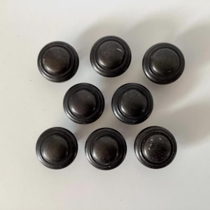 May include: A collection of eight dark bronze cabinet knobs. Each knob is round with a slightly domed center and a grooved edge. The knobs are arranged in a loose grid pattern against a white background.