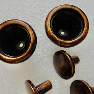 May include: A set of five antique brass cabinet knobs. The knobs have a round, flat top and a short, cylindrical stem. The knobs are in a distressed finish, giving them a vintage look.