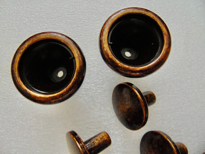 May include: A set of five antique brass cabinet knobs. The knobs have a round, flat top and a short, cylindrical stem. The knobs are in a distressed finish, giving them a vintage look.