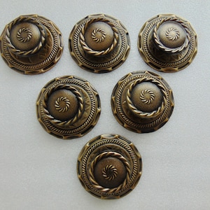May include: Six antique bronze-colored buttons. Each button has a raised spiral center, a rope-like border, and an outer decorative edge. The buttons are round and have a vintage aesthetic.