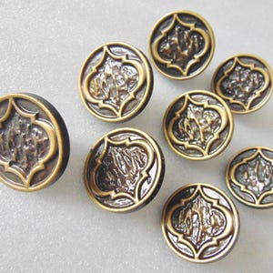 May include: A collection of antique-style buttons with a bronze finish. Each button features a raised, ornate design within a decorative border. The buttons are round and vary slightly in size, with a vintage aesthetic.