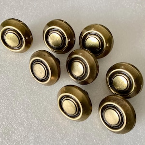 May include: A collection of eight antique brass cabinet knobs. Each knob features a circular design with a raised center and a decorative outer ring. The knobs have a warm, aged finish, suggesting vintage or retro style.