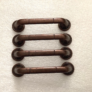 May include: Four antique-style bronze cabinet pulls. Each pull has a curved handle with decorative end pieces. The bronze finish has a slightly distressed appearance, adding to the vintage aesthetic. These pulls are designed for easy installation on cabinets or drawers.