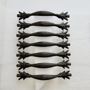 May include: Eight antique bronze cabinet pulls with a decorative floral design. Each pull has a curved shape and a textured finish.