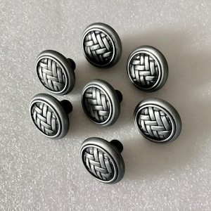 May include: A collection of eight silver-toned cabinet knobs. Each knob features a woven basket design on the face and a black stem. The knobs are round and have a slightly raised edge.