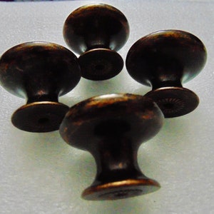 May include: Four antique bronze cabinet knobs with a round top and a small base. The knobs have a distressed finish.