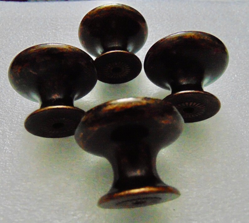 May include: Four antique bronze cabinet knobs with a round top and a small base. The knobs have a distressed finish.