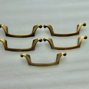 May include: Five antique brass drawer pulls with a curved handle design. The pulls have a warm, aged finish, and the ends curl upwards. These hardware pieces are ideal for adding a vintage touch to furniture.