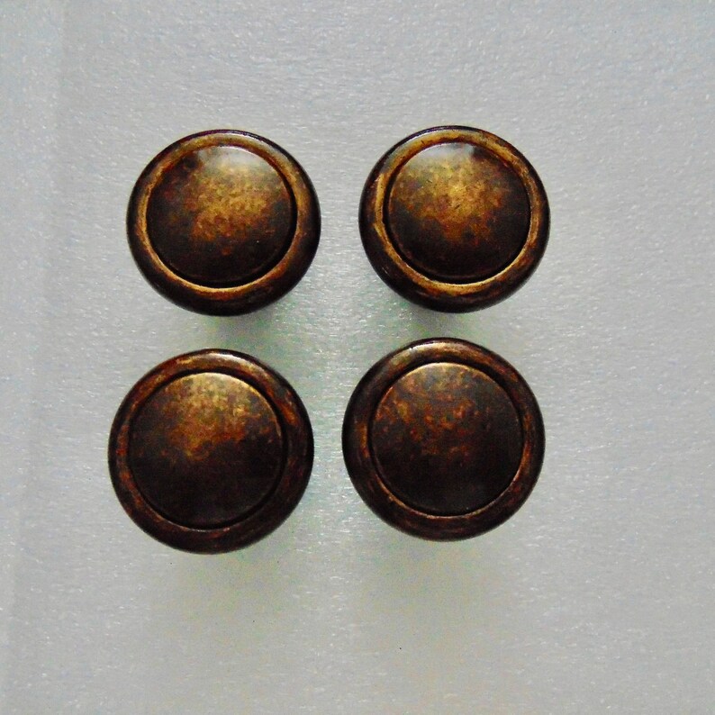 May include: Four round, bronze-colored cabinet knobs with a slightly raised edge around the perimeter.