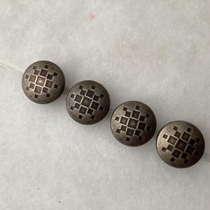 May include: Four circular metal buttons with a dull silver finish, each featuring an identical engraved geometric pattern consisting of a central square surrounded by smaller squares arranged in a cross-like formation on the button face.