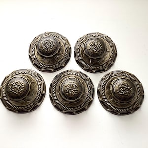 May include: Five antique bronze-colored decorative buttons with intricate floral and rope-like detailing. Each button features a central raised design and a detailed outer edge, perfect for craft projects.