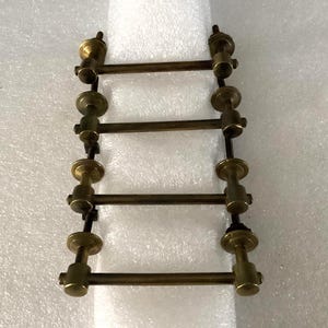 May include: A set of six antique brass clock parts. Each part has a series of horizontal bars connected by vertical posts with decorative circular accents. The brass has a warm, aged patina.