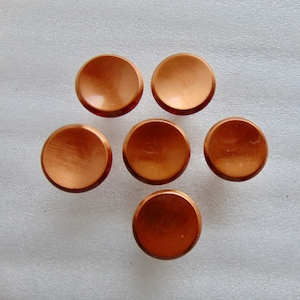 May include: Six copper-colored, round cabinet knobs arranged in a circular pattern. Each knob has a brushed metal finish, reflecting light. The knobs are evenly spaced and appear to be new.