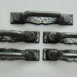 May include: Five antique-style cabinet pulls with a distressed, hammered metal finish. The handles are a dark gray color with lighter highlights, and each has a rectangular backplate with decorative edges. These pulls are suitable for furniture restoration or new builds.