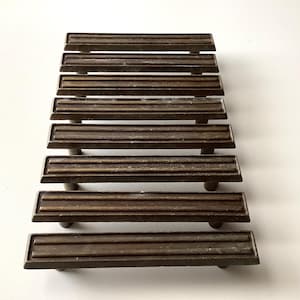 May include: Set of seven vintage bronze-toned drawer pulls. Each pull features a rectangular face with three horizontal grooves and a rounded base. These hardware pieces are ideal for furniture restoration projects.