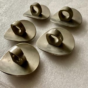 May include: Five silver ring holders, each with a unique design, are arranged on a white surface. The holders are made of a smooth, reflective metal and have a simple, modern aesthetic.
