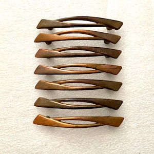 May include: Seven bronze-toned cabinet pulls arranged vertically. Each pull has a curved, elongated design with a central opening. The pulls are made of metal and have a warm, metallic finish, suitable for furniture restoration or new builds.