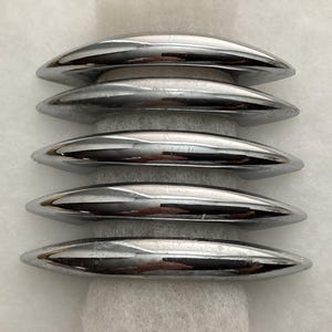 May include: Five polished chrome cabinet pulls arranged in a vertical stack. Each handle features a smooth, arched, crescent-like shape with a reflective metallic finish. The hardware is uniform in size and design, showcasing a sleek, curved profile.