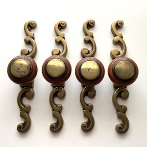 May include: Four antique cabinet pulls. Each pull features a round, wooden knob with a brass center and decorative brass hardware. The pulls have a warm, vintage aesthetic, perfect for adding character to furniture.