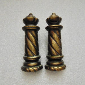 May include: Two antique bronze-colored finials with a twisted rope design. Each finial has a decorative top and base, and they are displayed against a neutral background. These decorative elements are likely for furniture or architectural use.