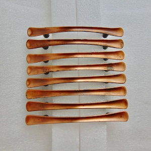 May include: A set of eight horizontal cabinet pulls with a curved, elongated shape and a metallic copper finish. Each handle features a smooth, slightly concave center section that tapers toward the ends, mounted on two small dark circular posts.