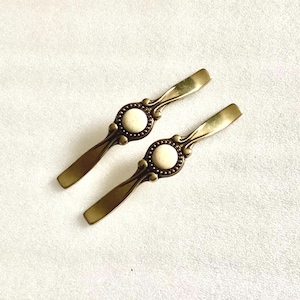 May include: Two antique-style cabinet pulls with ornate metalwork and white ceramic accents. The pulls are in a brass finish.