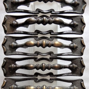 May include: Five antique brass cabinet door pulls with ornate designs. Each pull has a decorative knob in the center and a curved handle on either side. The pulls are arranged in a vertical stack.