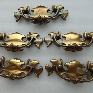 May include: Set of four antique brass cabinet pulls with ornate, leaf-shaped designs. Each pull has a curved handle and a decorative center.