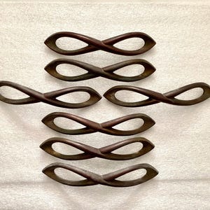 May include: Seven dark brown, infinity-shaped wooden handles. The handles are arranged in a grid pattern against a white background. Each handle has a smooth, curved design, with a slightly textured surface.