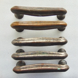 May include: Five antique cabinet door pulls with a curved design. The pulls are made of metal and have a distressed finish in shades of brown, silver, and green.