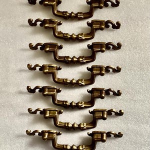 May include: Set of six antique brass drawer pulls with ornate scrollwork and a decorative design. The pulls are in excellent condition and would be a great addition to any vintage or antique furniture.
