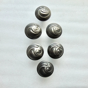 May include: Six antique-style cabinet knobs with a swirling design. The knobs are a dark, metallic gray color and have a rounded shape. They are arranged in a vertical pattern against a white background.