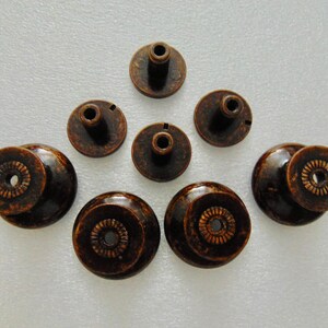 May include: Eight antique bronze cabinet knobs with a decorative design. The knobs have a round base and a raised center with a small hole in the center.