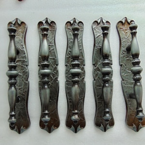 May include: Five ornate metal drawer pulls with a distressed, aged finish. Each pull features a decorative design with a scroll-like top and a rounded bottom. The pulls are a dark gray color with hints of green and brown.