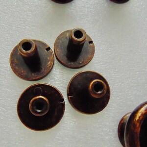 May include: Five antique bronze cabinet knobs with a round base and a raised center post. The knobs have a distressed finish and a slightly worn look.