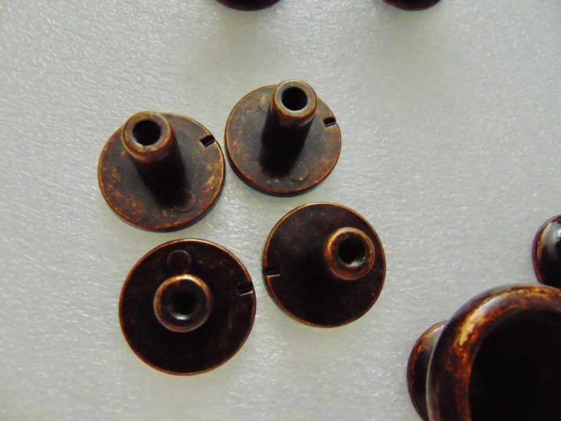 May include: Five antique bronze cabinet knobs with a round base and a raised center post. The knobs have a distressed finish and a slightly worn look.