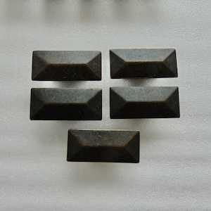 May include: Five bronze-colored, rectangular cabinet knobs with a faceted design. The knobs have a slightly aged appearance, suggesting a vintage or antique style. The hardware is arranged on a white surface.